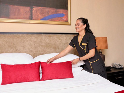 Picture of a maid making a bed at the Costa Rica Medical Center Inn, San Jose, Costa Rica.  The bed shows cherry red pillows against a white bed sheet.