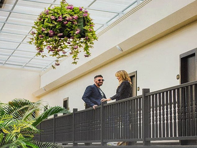 26-	Picture of an interior corridor at the Costa Rica Medical Center Inn, San Jose, Costa Rica.  The picture shows a happy couple on the second floor framed by an overhead hanging plant.